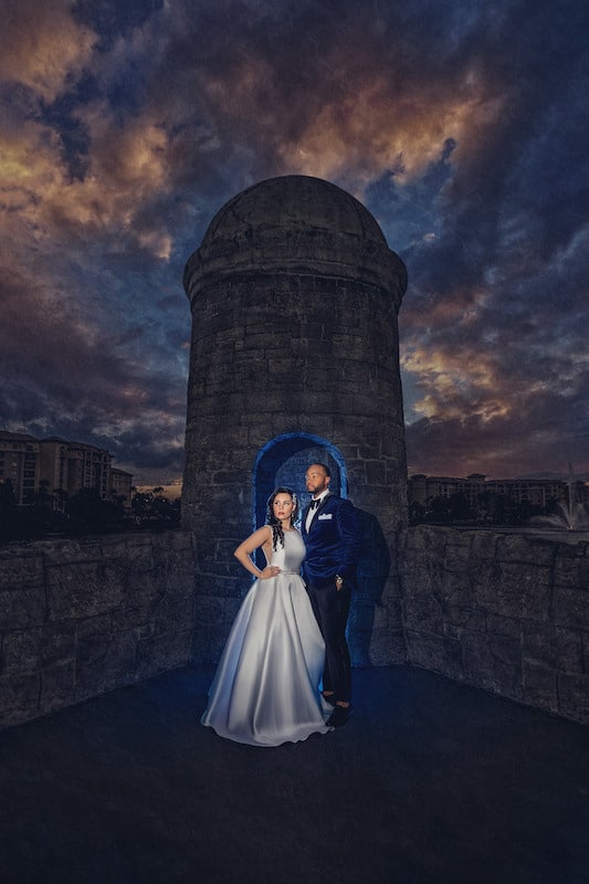 bride and groom standing on old structure with blue light behind them