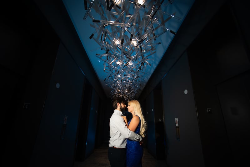 man and woman hugging in hallway with decorative chandelier running along the ceiling