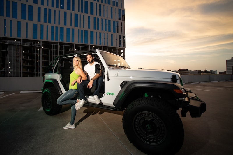 man and woman with arms linked sitting inside of white jeep in a parking garage