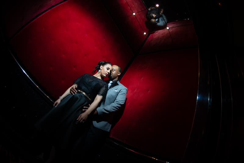 man and woman standing in an elevator lined with red velvet and mirrors on the ceiling