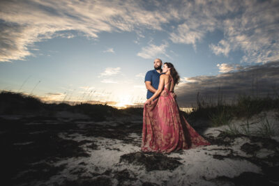 man and woman standing next to beach dunes at sunset