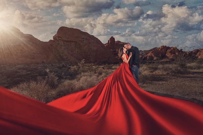 woman in a long red dress kissing a man in the desert