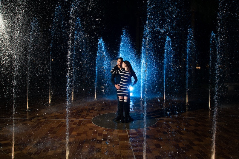 man and woman standing in middle of water fountain with blue light shining through water