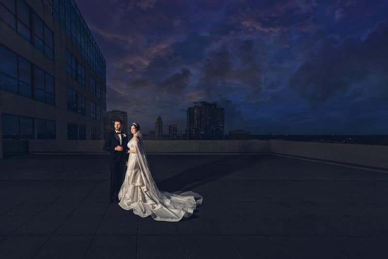 bride and groom standing outside on balcony just after sunset