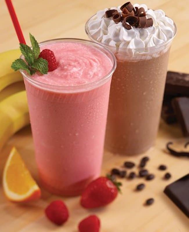 chocolate and strawberry milkshakes set on a table surrounded by fresh fruit and pieces of chocolate