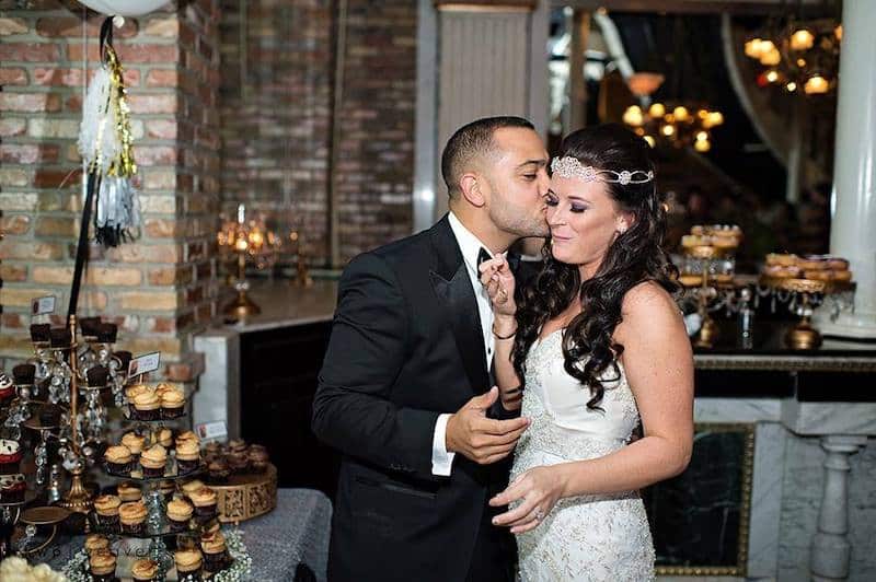 groom kissing his bride on the cheek while they stand next to the dessert table filled with cupcakes