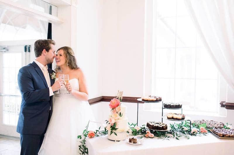 bride and groom toasting each other with champagne while standing next to dessert table