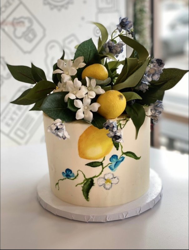 wedding cake decorated with real flowers and lemons on top, and similar images painted onto side of cake
