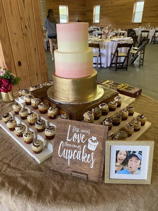 wedding cake surrounded by cupcakes and a sign that reads first comes love then comes cupcakes