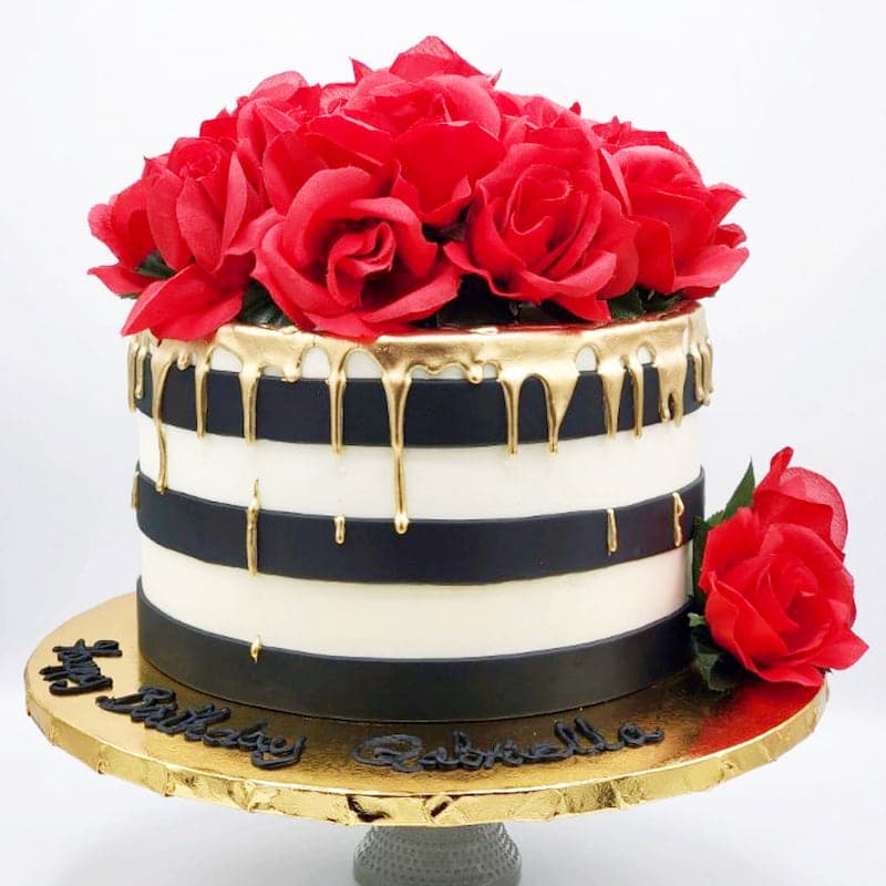 large cake with white and black stripes, gold dripping from the top and covered with red roses