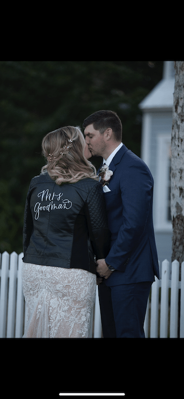 bride kissing her groom while wearing a leather jacket with her new married name stitched on the back by Bare Lettered Calligraphy