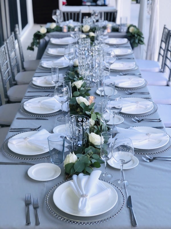 long table decorated for wedding reception with grey linen and chairs and white plates