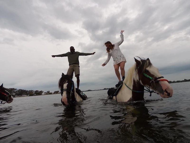 man and woman standing on horses as they wade through chest high water