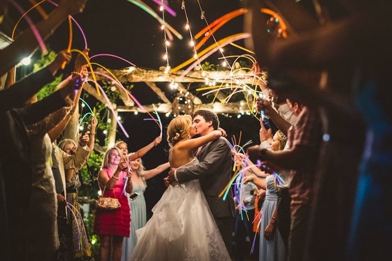 bride and groom kissing while guests wave multi-colored glow sticks around