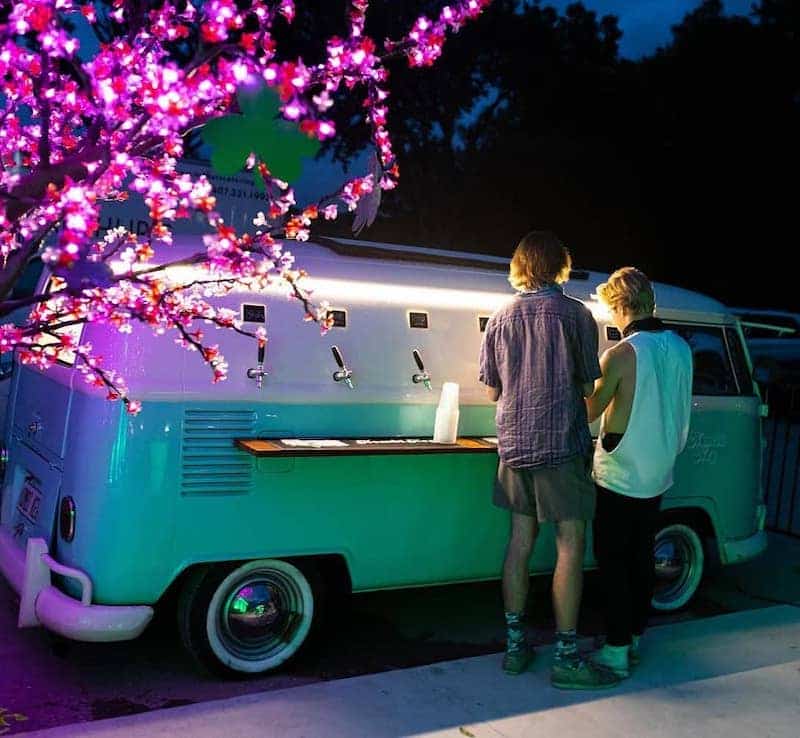friends pouring a drink from the Kombi Keg Volkswagen van at night under fuschia lights