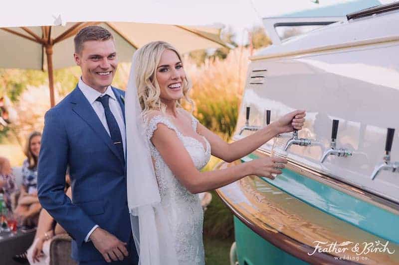 bride and groom smiling as they pour a drink from the kombi keg volkswagen van