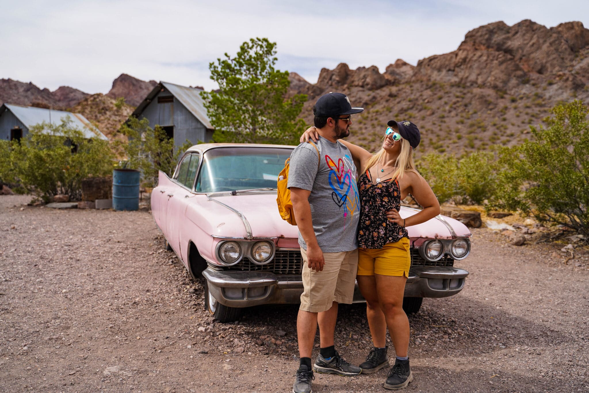 newly engaged couple standing in front of an old car on a dirt road