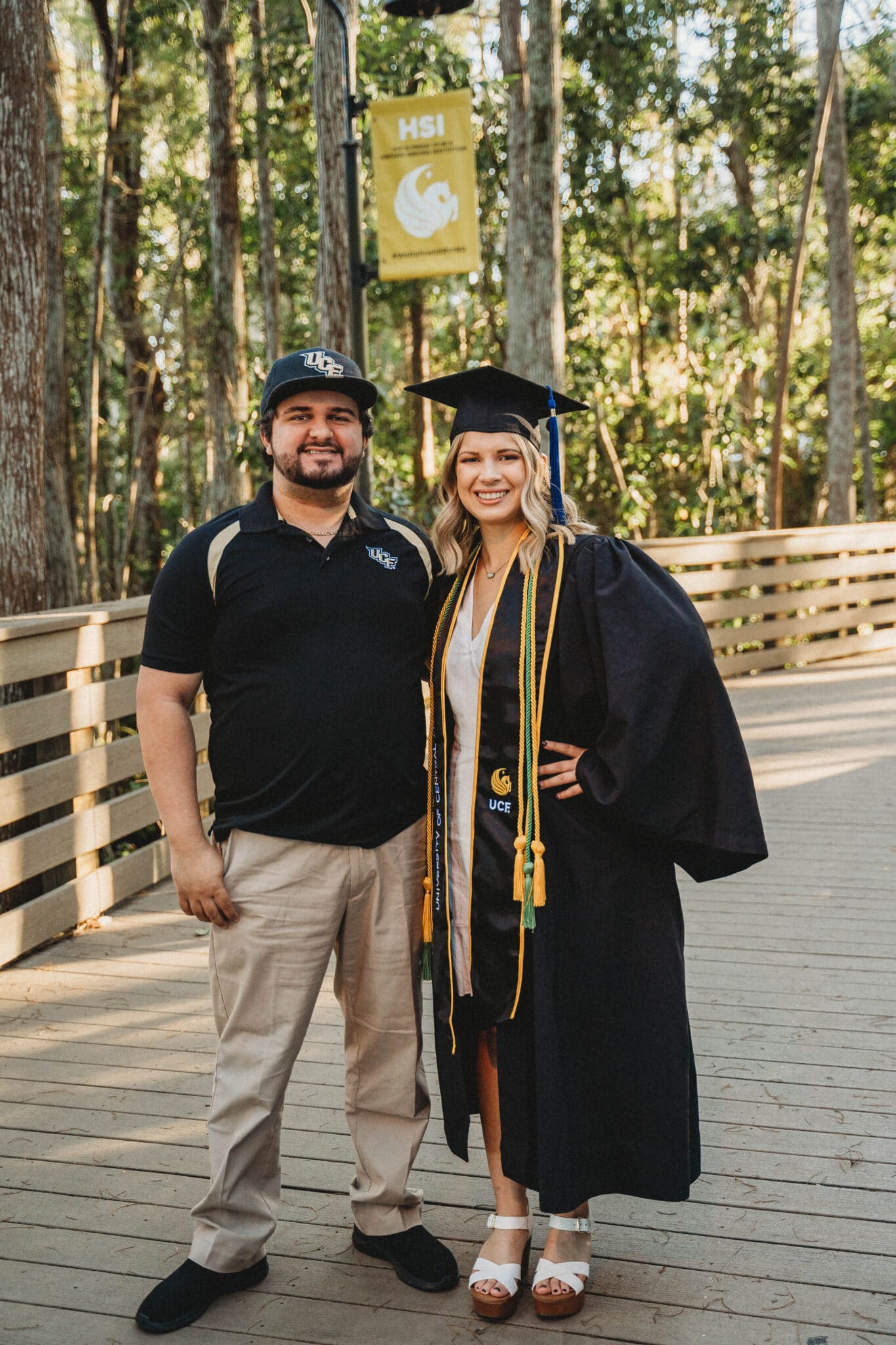 couple standing next to each other at the university of central florida with the bride to be in a cap and gown