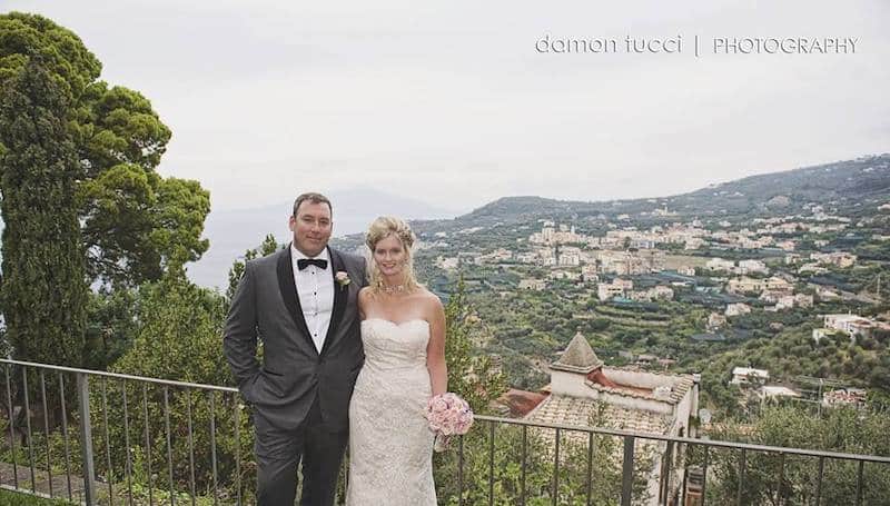 bride and groom leaning on a rail on a hill overlooking a city below them