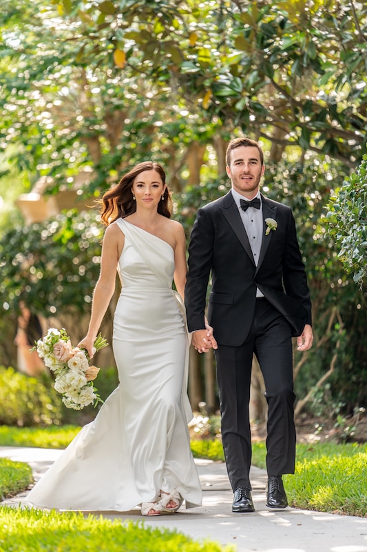 bride and groom walking hand in hand down a curved sidewalk