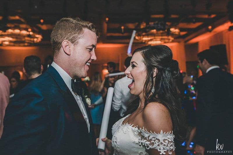 bride laughing with her groom as she holds a foam light stick during their wedding reception