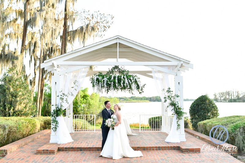 bride and groom standing on a covered pavilion overlooking a large lake