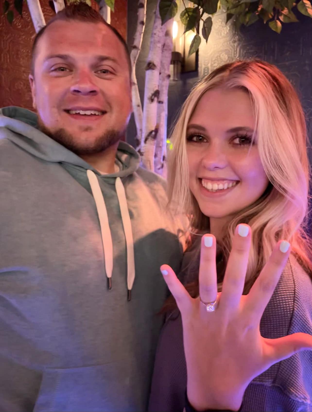 bride and groom to-be showing off new engagement ring at their romantic home marriage proposal