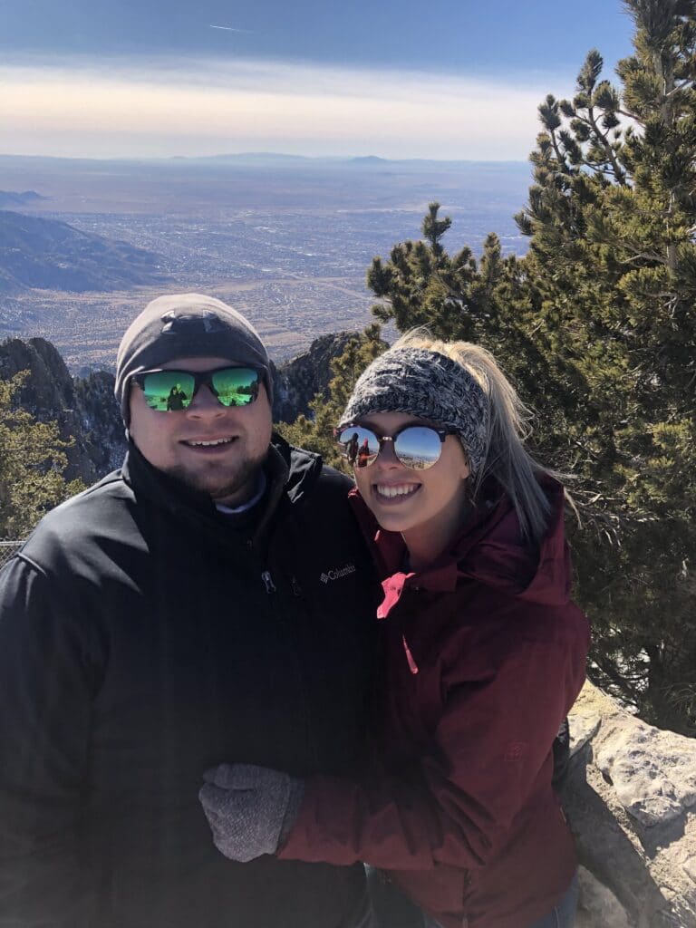newly engaged couple on a mountain bundled up in warm clothes with a valley view behind them
