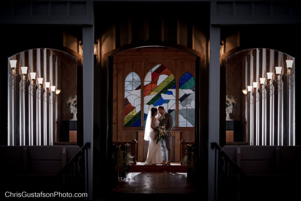bride and groom embracing in front of large stain glass window at Chapel Valley Farm