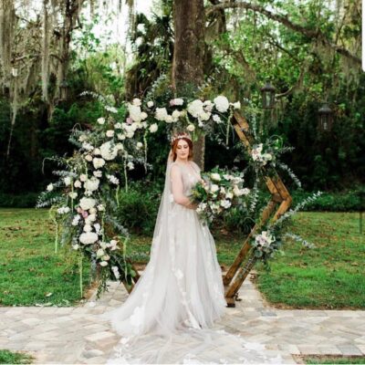 bride standing in front of wooden hexagon covered in white and green floral garland