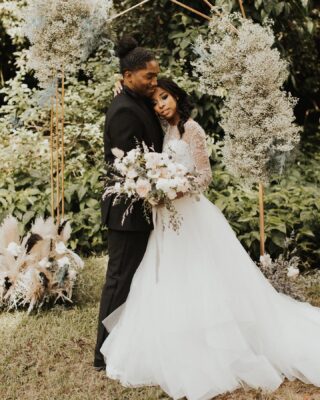 bride holding white bouquet and looking at camera while resting head on grooms chest