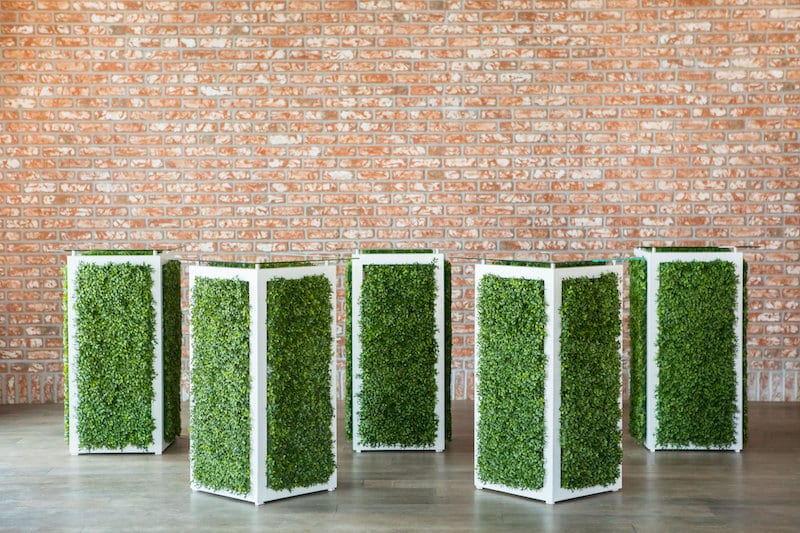5 high top glass tables with green vine walls on the table stands provided by CHIC Event Furniture Rental