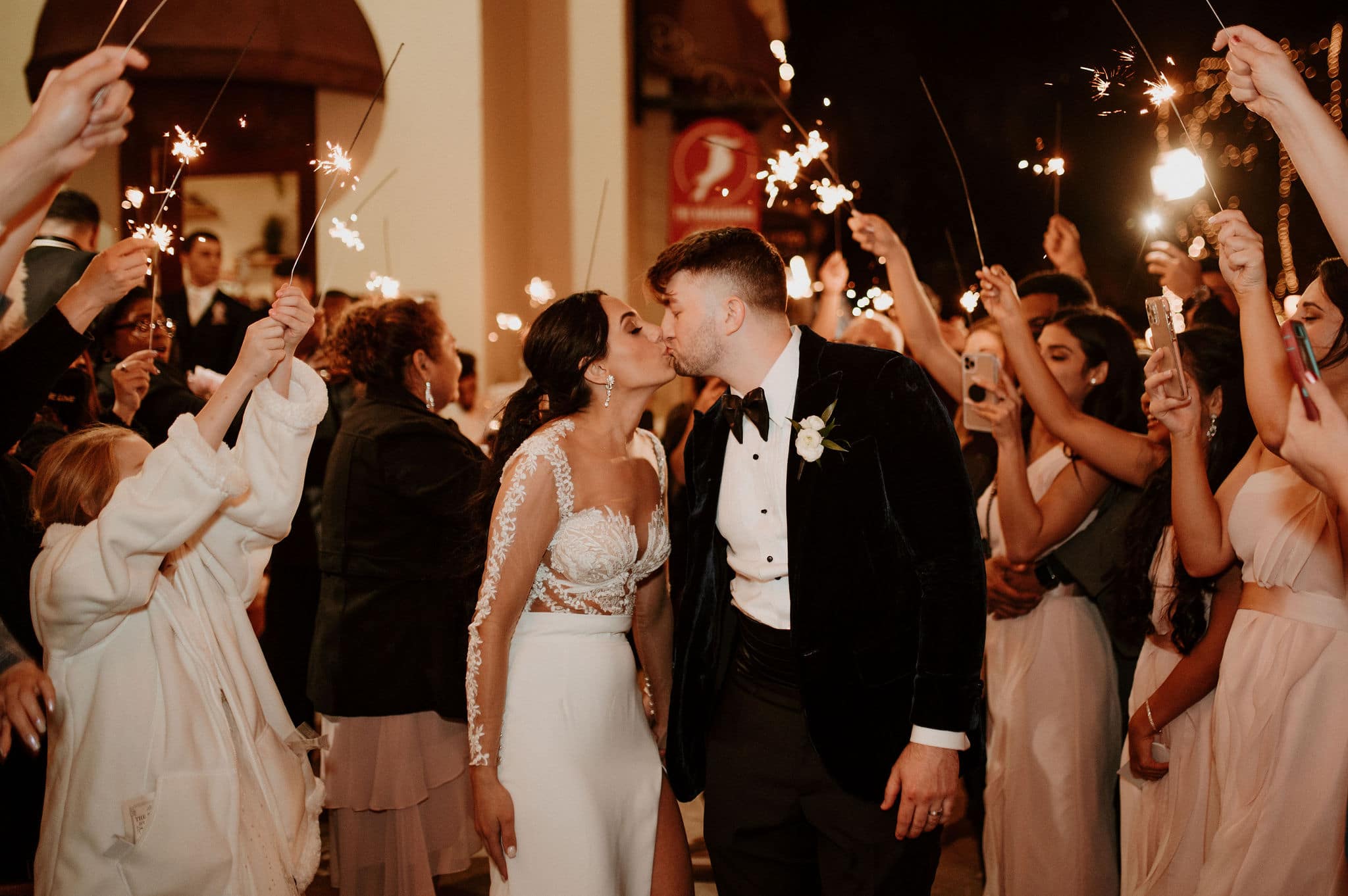 newly married couple kissing after leaving their st. augustine winter wedding with guests waving sparklers around them