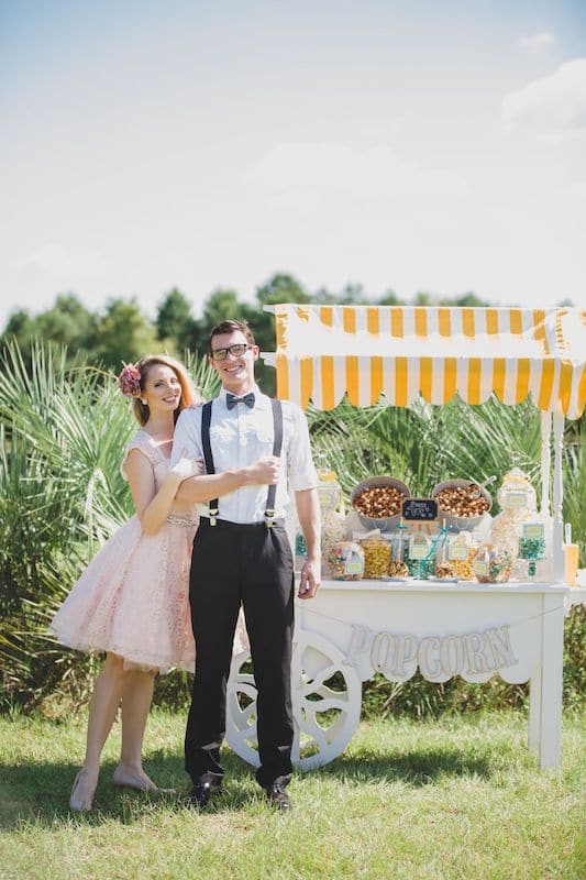 bride and groom standing next to a popcorn stand set up outside