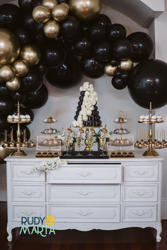 dessert table from Florida Candy Buffets decorated with black and gold balloons that match the desserts