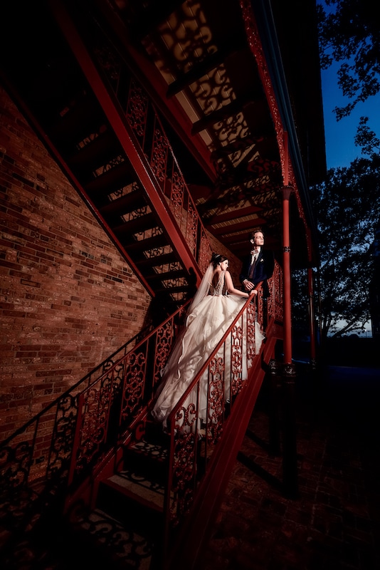 bride and groom walking up steps along the side of a building by Lazzat Photography