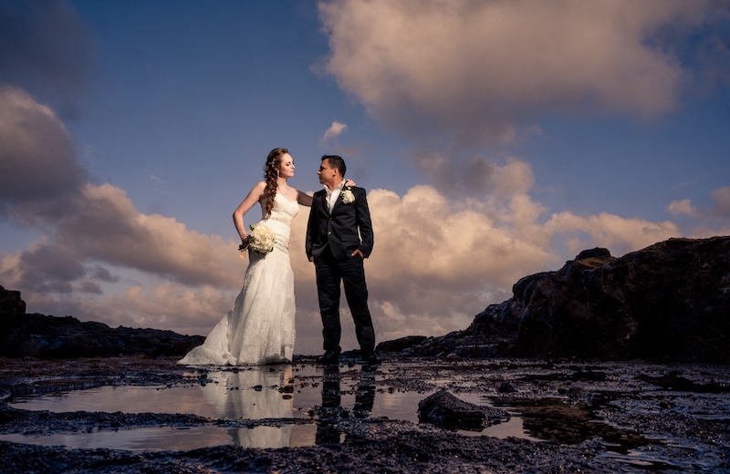 bride and groom standing on a beach by Lazzat Photography