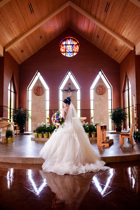 bride standing in large church holding her bouquet by Lazzat Photography