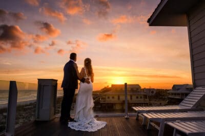 bride and groom standing on a balcony watching the sun set by Lazzat Photography