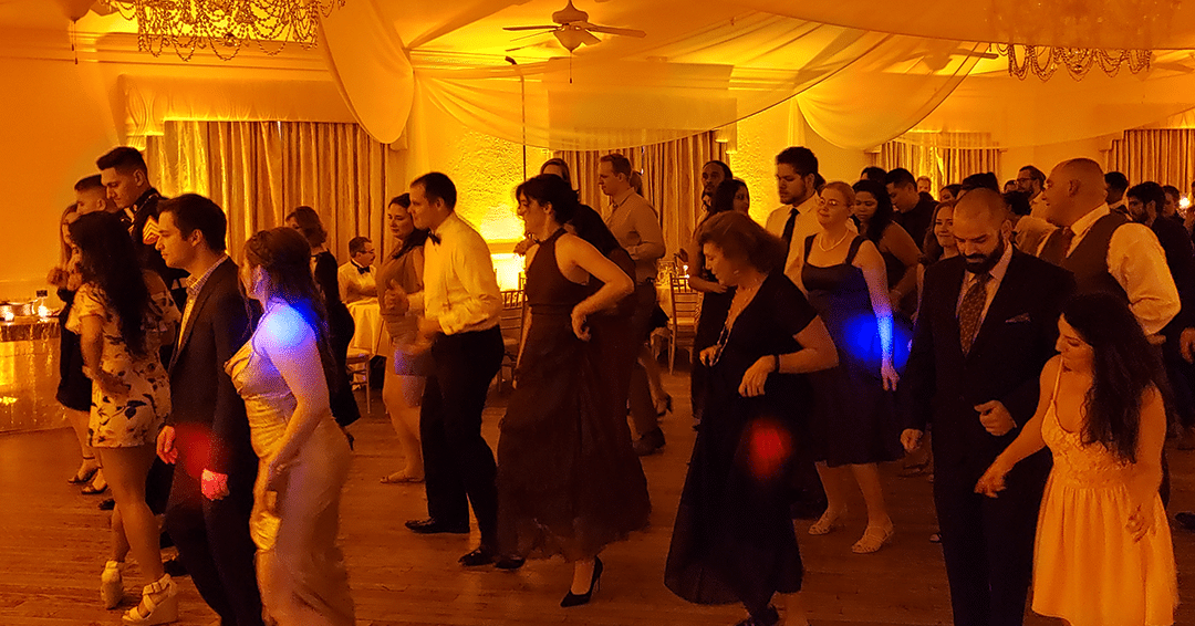 wedding guests at reception line dancing in ballroom with gold uplighting