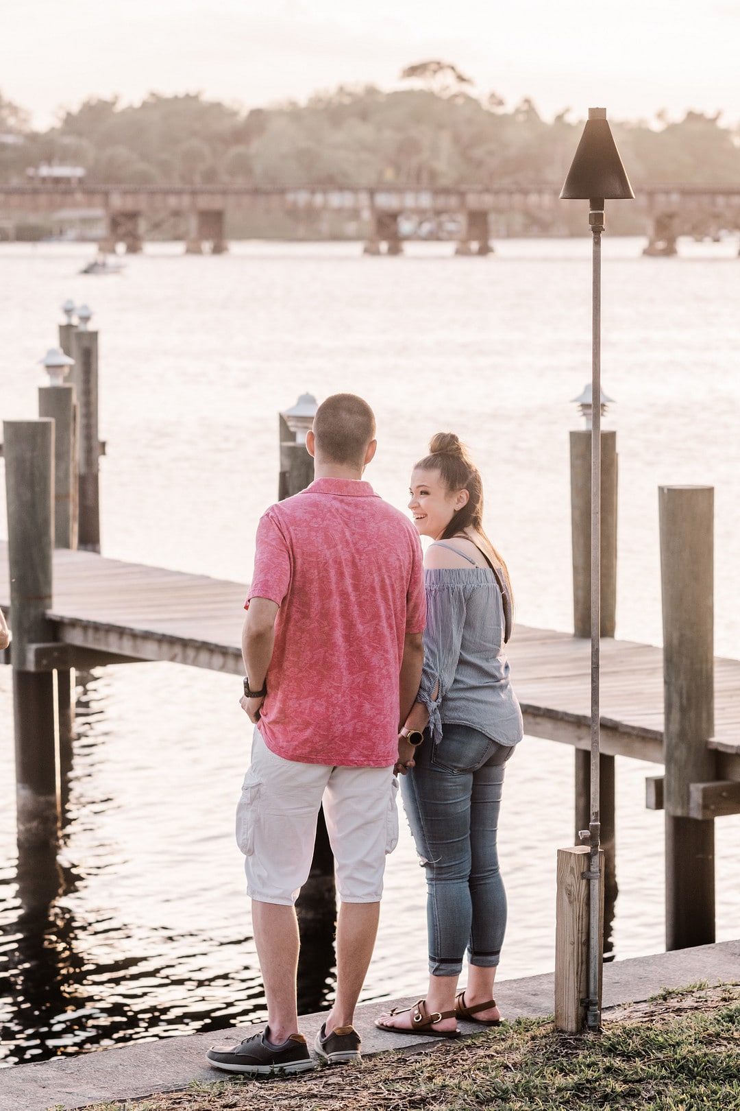 newly engaged couple standing near the water next to dock