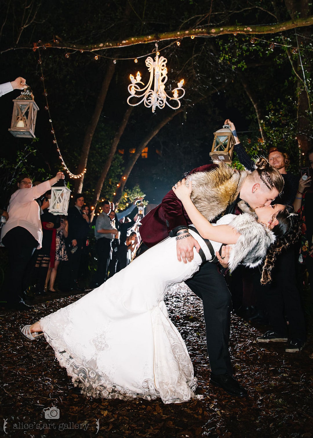 groom kisses bride and dips her down in front of guests holding lanterns during outdoor wedding reception grand exit