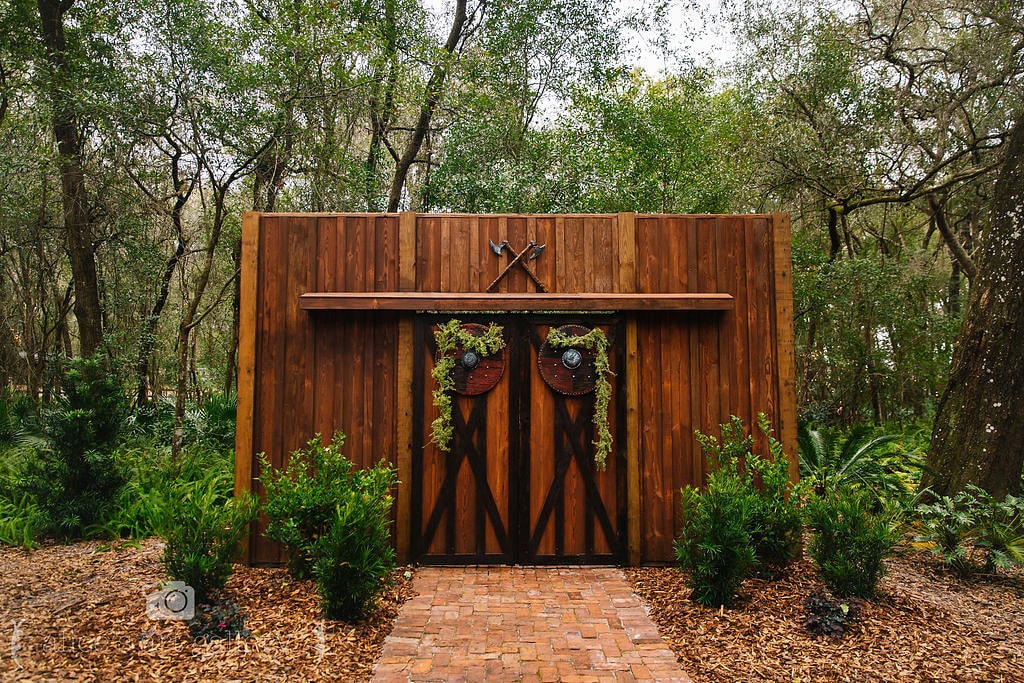 giant wood barn doors decorated with garland and two axes above the doors with green plants in front and trees in the background