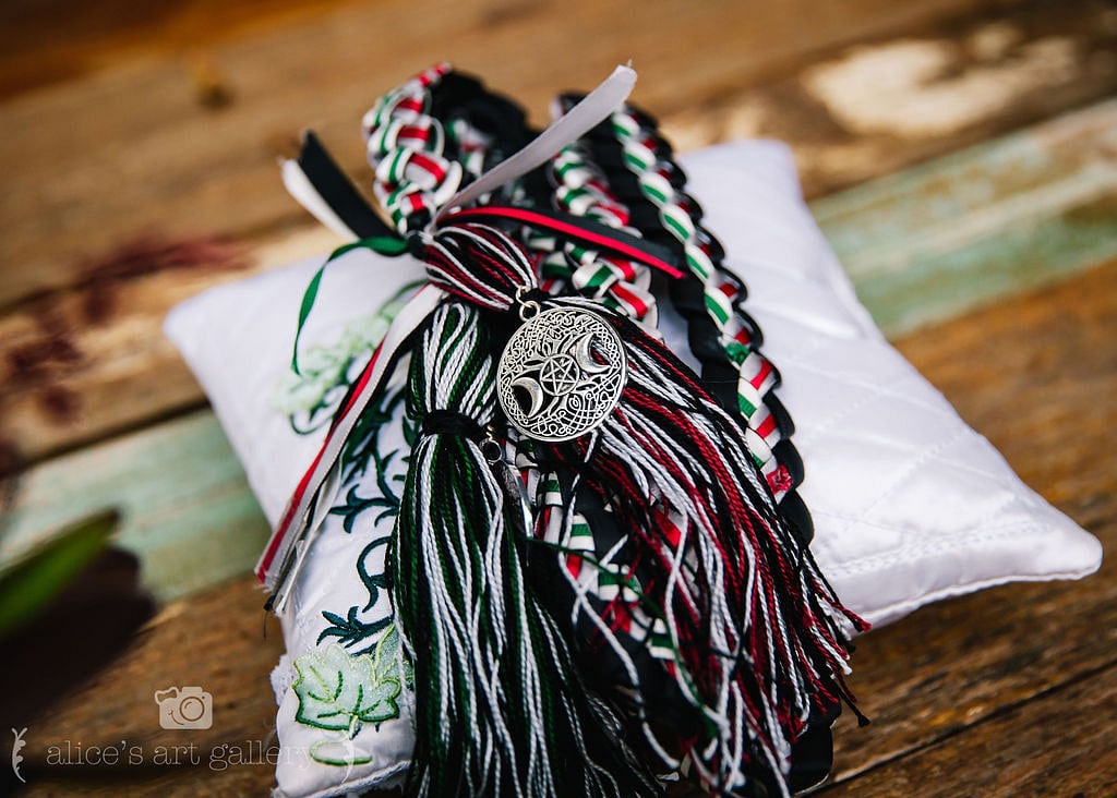 braided white green red and black cords for wedding ceremony lay together on top of small white pillow