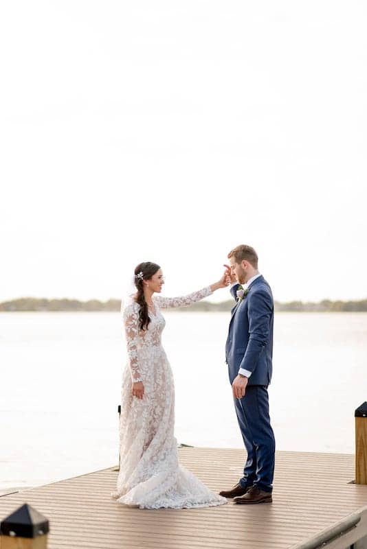 bride and groom standing on a dock on a large lake