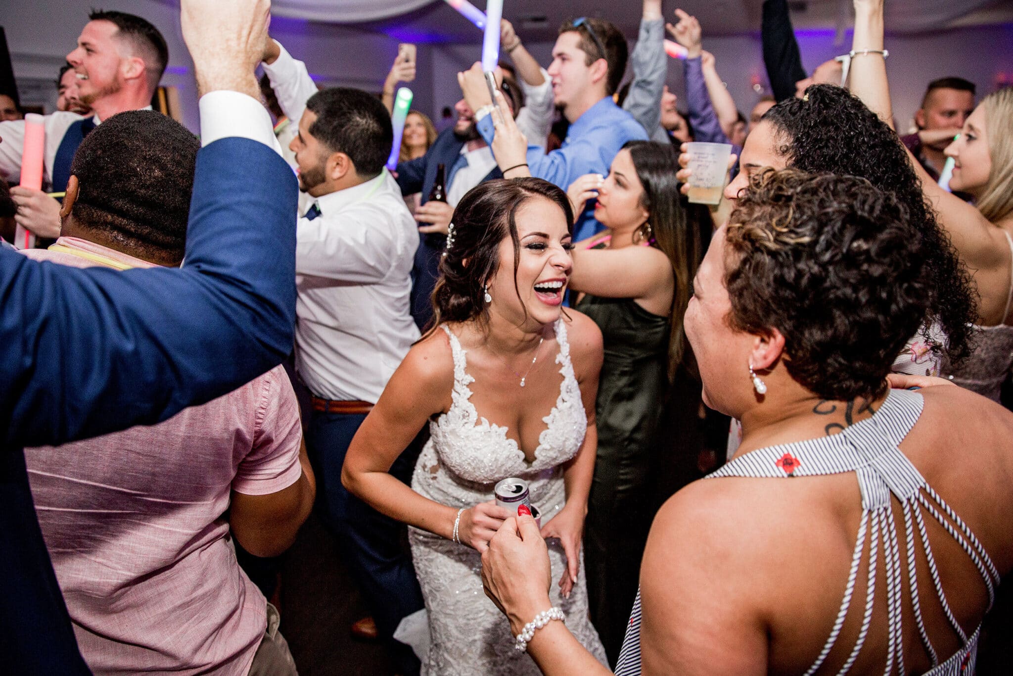bride laughing with drink in hand in the middle of guests dancing at wedding reception