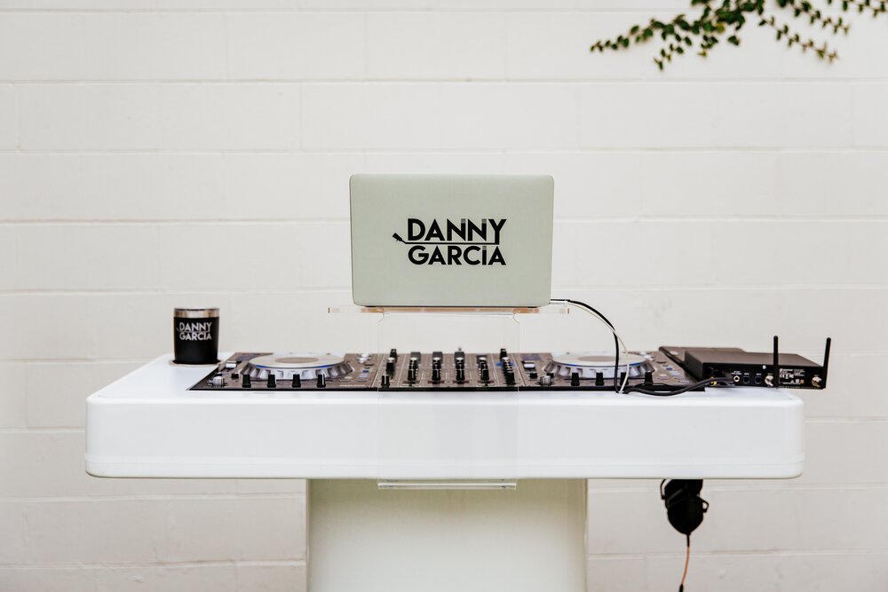 dj booth setup in front of white wall with laptop and custom sticker for danny garcia on the stand