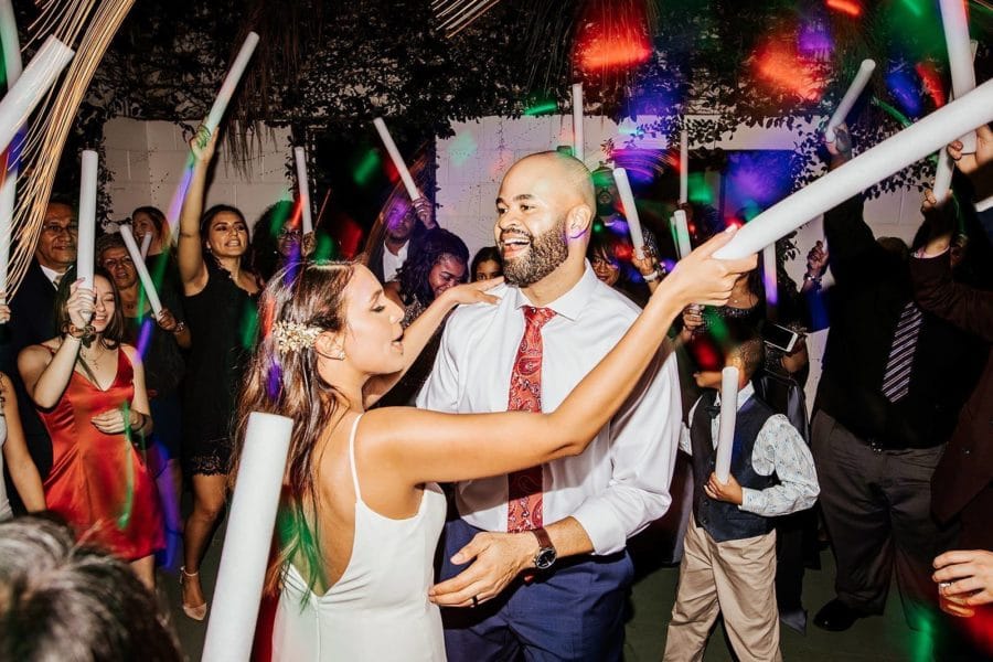 bride and groom dance with each other at wedding reception while guests dance around them with different colored light up foam sticks