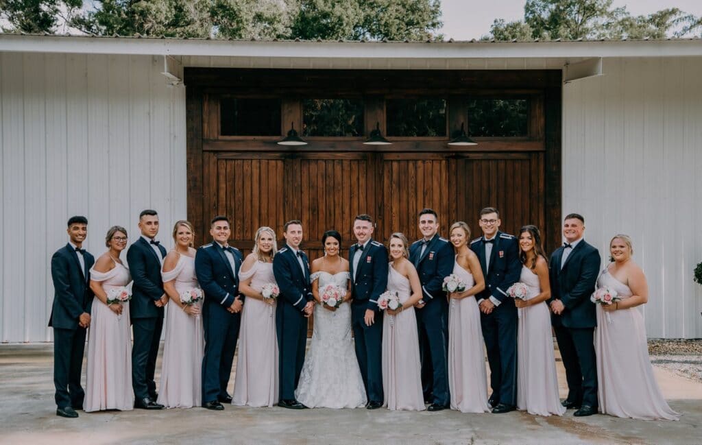 bride and groom standing with their large bridal party outside of Cypress Creek Farmhouse