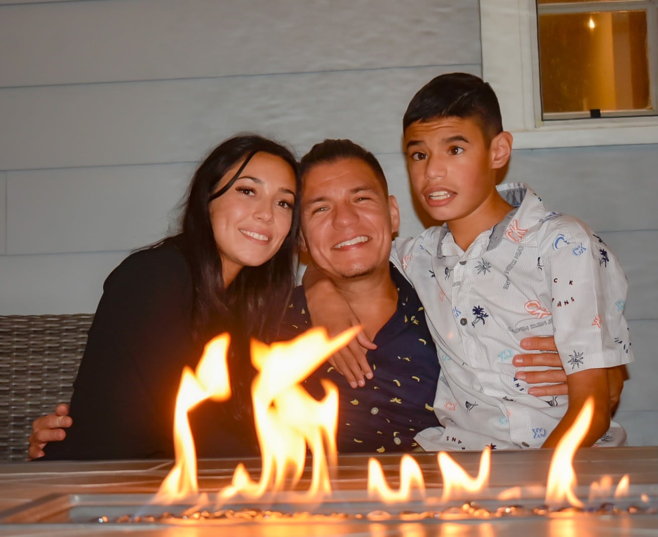 newly engaged couple with their son hugging around a fire